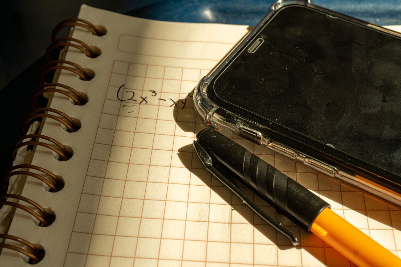 embark A notebook with a math equation, smartphone, and pen on checkered paper in warm lighting.