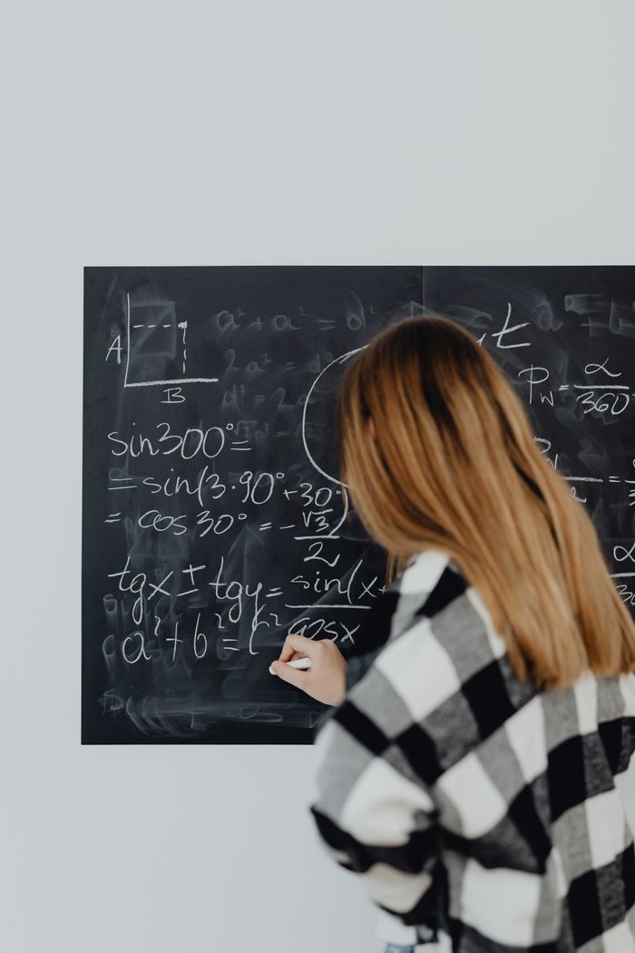 gallery-03 Teenage girl solving math equations on a chalkboard in classroom.