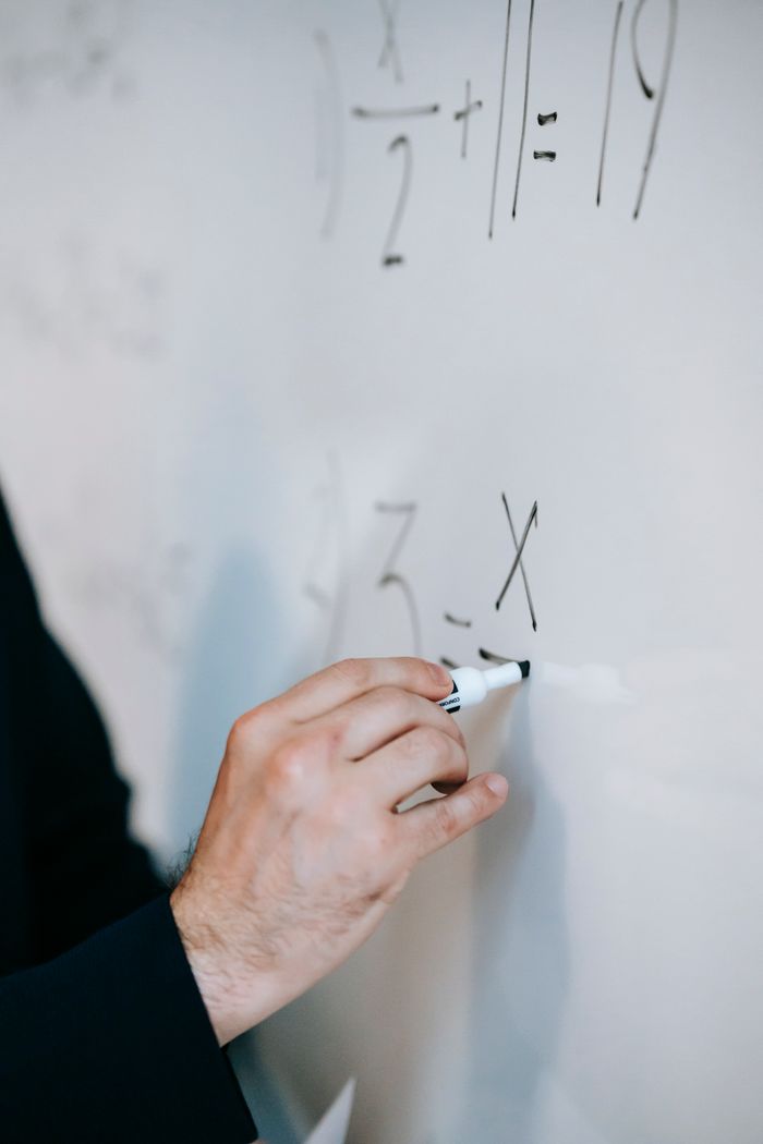 gallery-01 An educator uses a marker to solve equations on a whiteboard, demonstrating math skills.